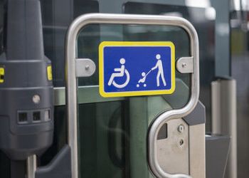 A blue and yellow accessibility sign on a train door showing symbols for a wheelchair user and a person pushing a pram.